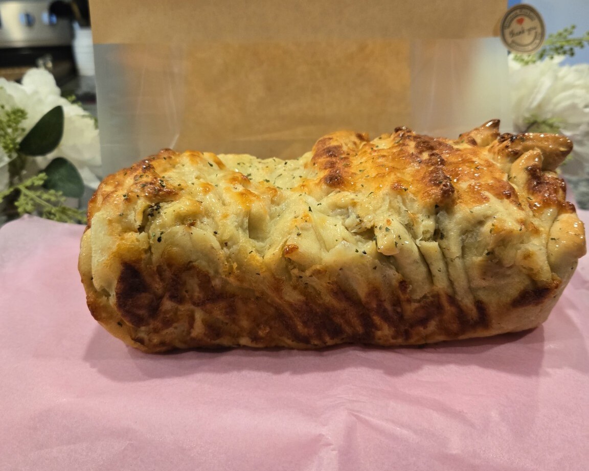 Garlic butter cheese pull-apart bread on pink paper with a kraft bakery bag behind it