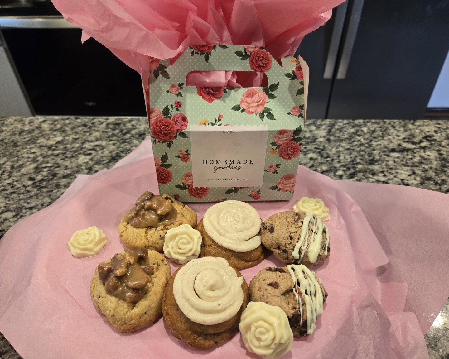Six assorted cookies and white chocolate roses arranged around a floral gift box filled with pink tissue paper